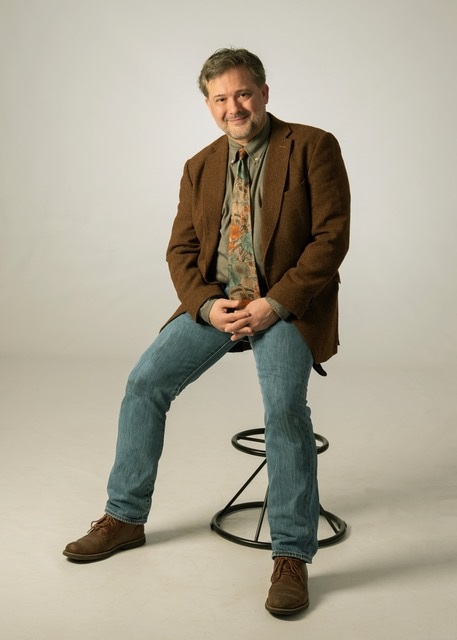 Dr. Richard Z: Gallant sitzt in einem braunen Jackett vor einem weißen Hintergrund und lächelt in die Kamera.