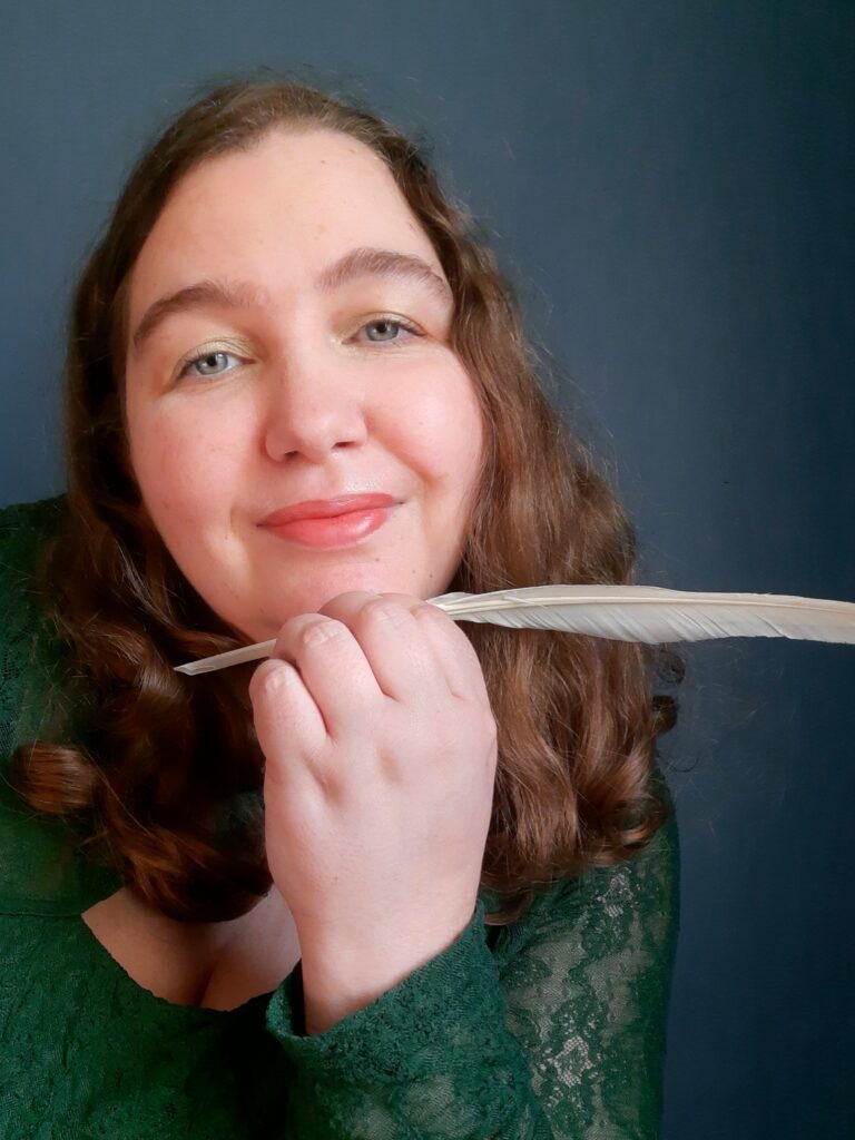 Lena Richter: Person mit mittelbraunen Haaren und grünem Oberteil aus Spitze, eine Hand mit weißer Feder vor dem Kinn.